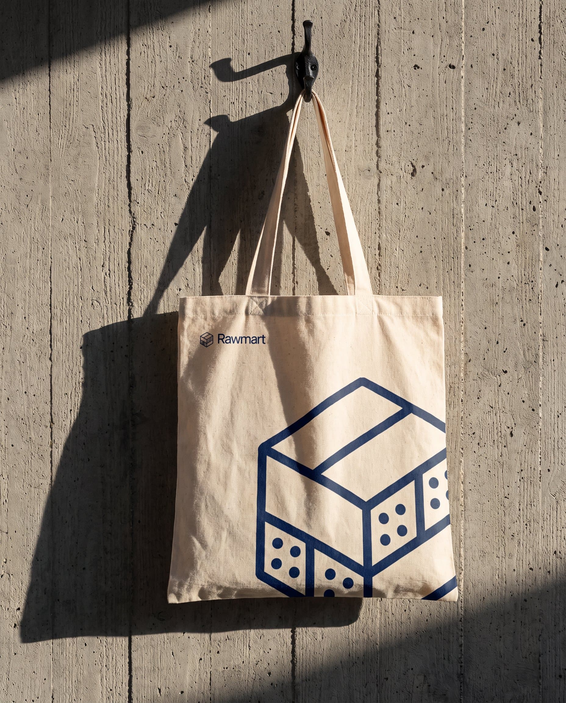 A canvas tote printed with the Rawmart module, hanging on a concrete wall
