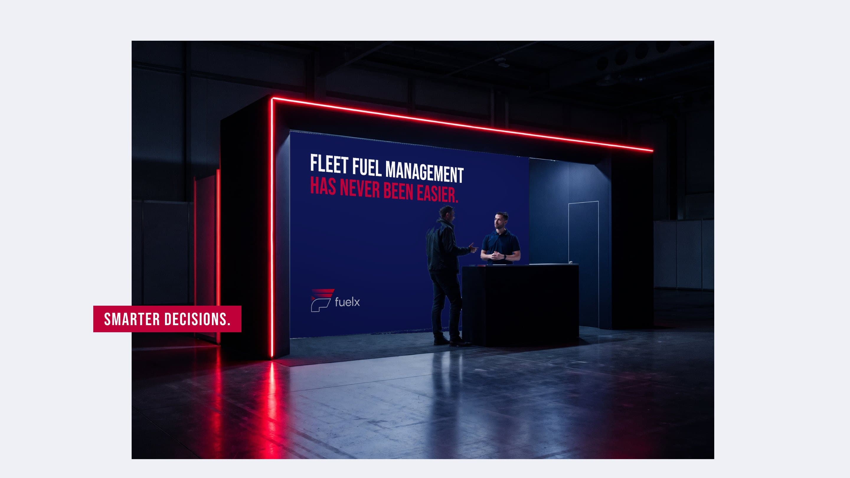 A fleet operator at the dark Fuelx stand of a trade show, lined in red neon, Fleet fuel management has never been easier. on its navy wall, a Smarter decisions tab across the photograph