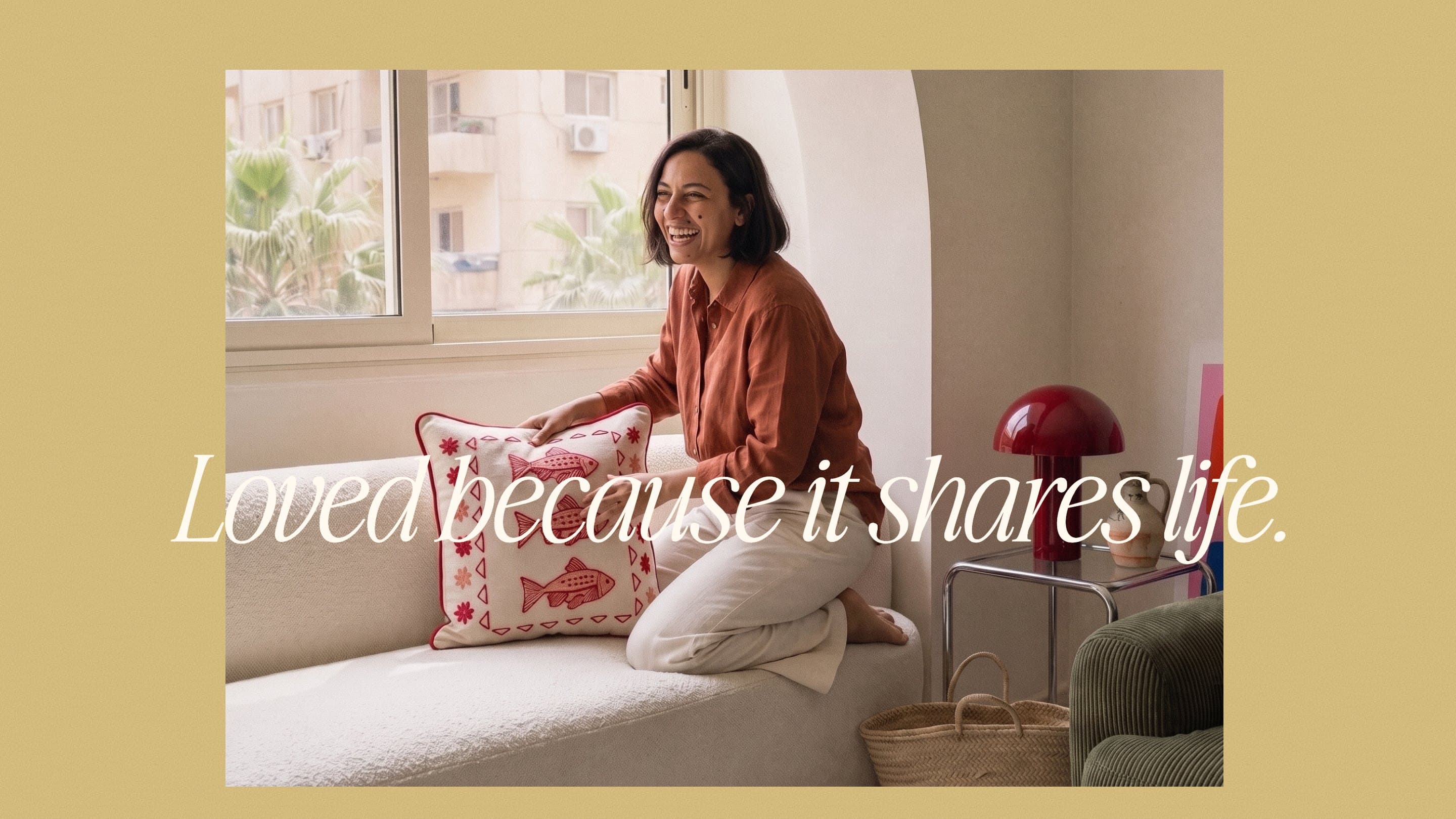 A woman laughs on a sofa in a Cairo apartment with the Three Fish Cushion: Loved because it shares life