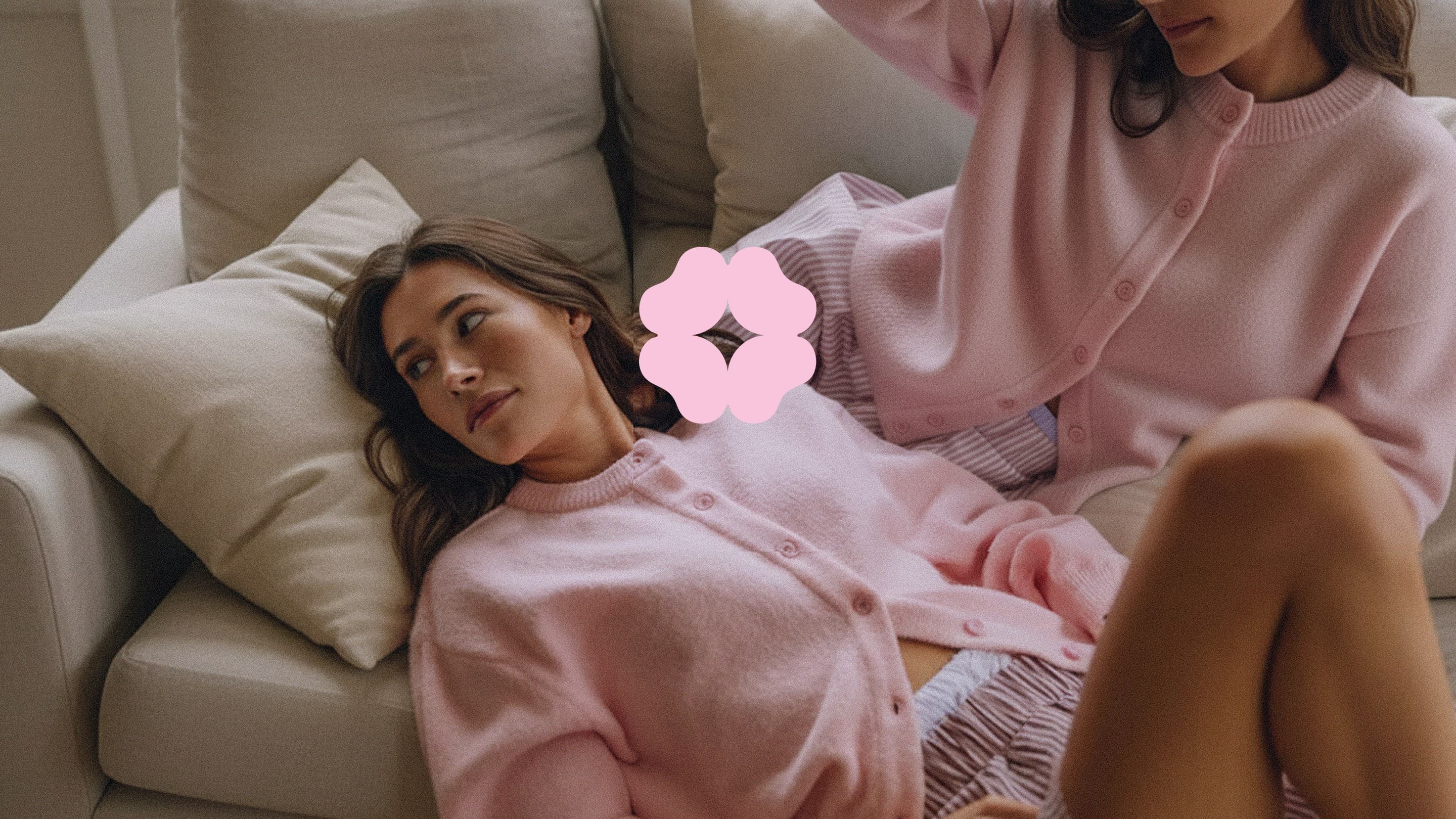 Two women in pink knits on a cream sofa, the Shishis flower between them