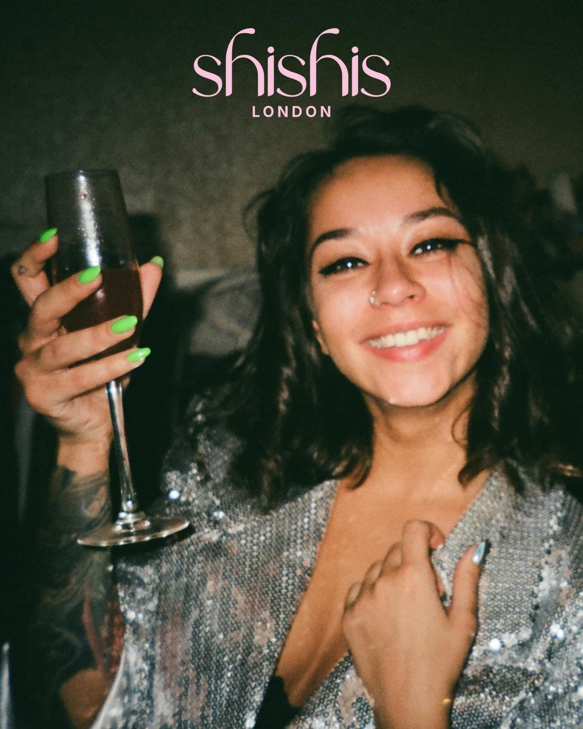 A woman in silver sequins raises a glass of champagne, the shishis London wordmark above her