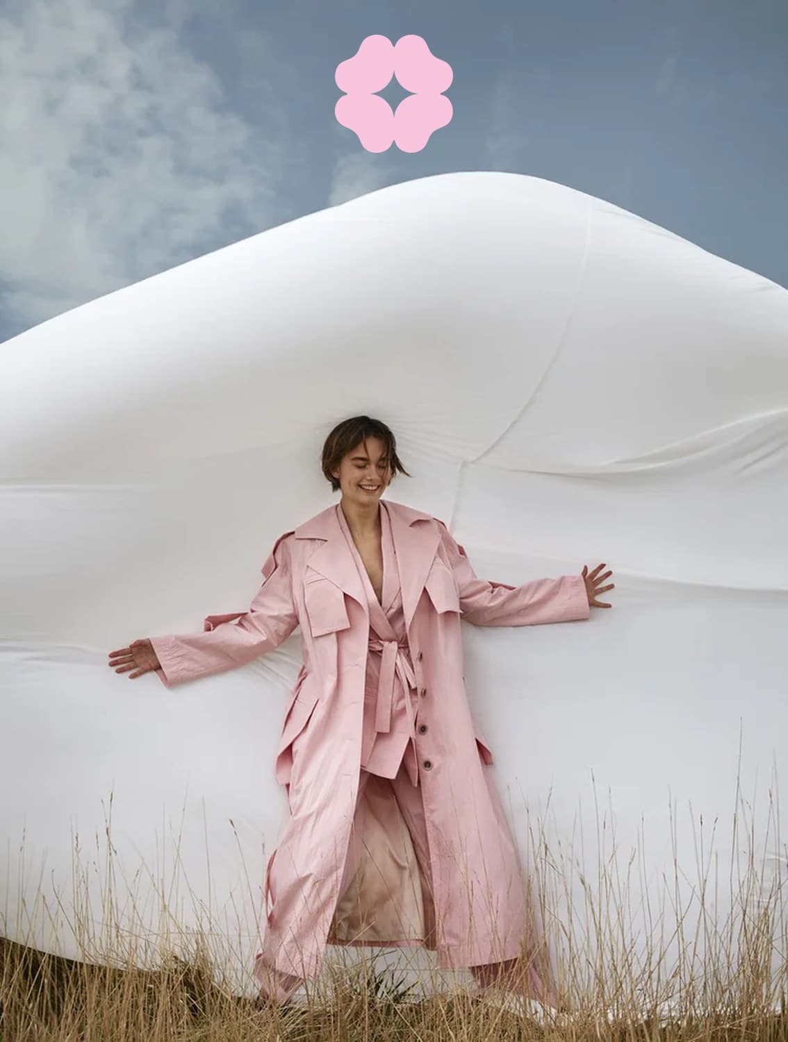 A woman in a pink trench coat against a white inflatable, the Shishis flower in the sky above her
