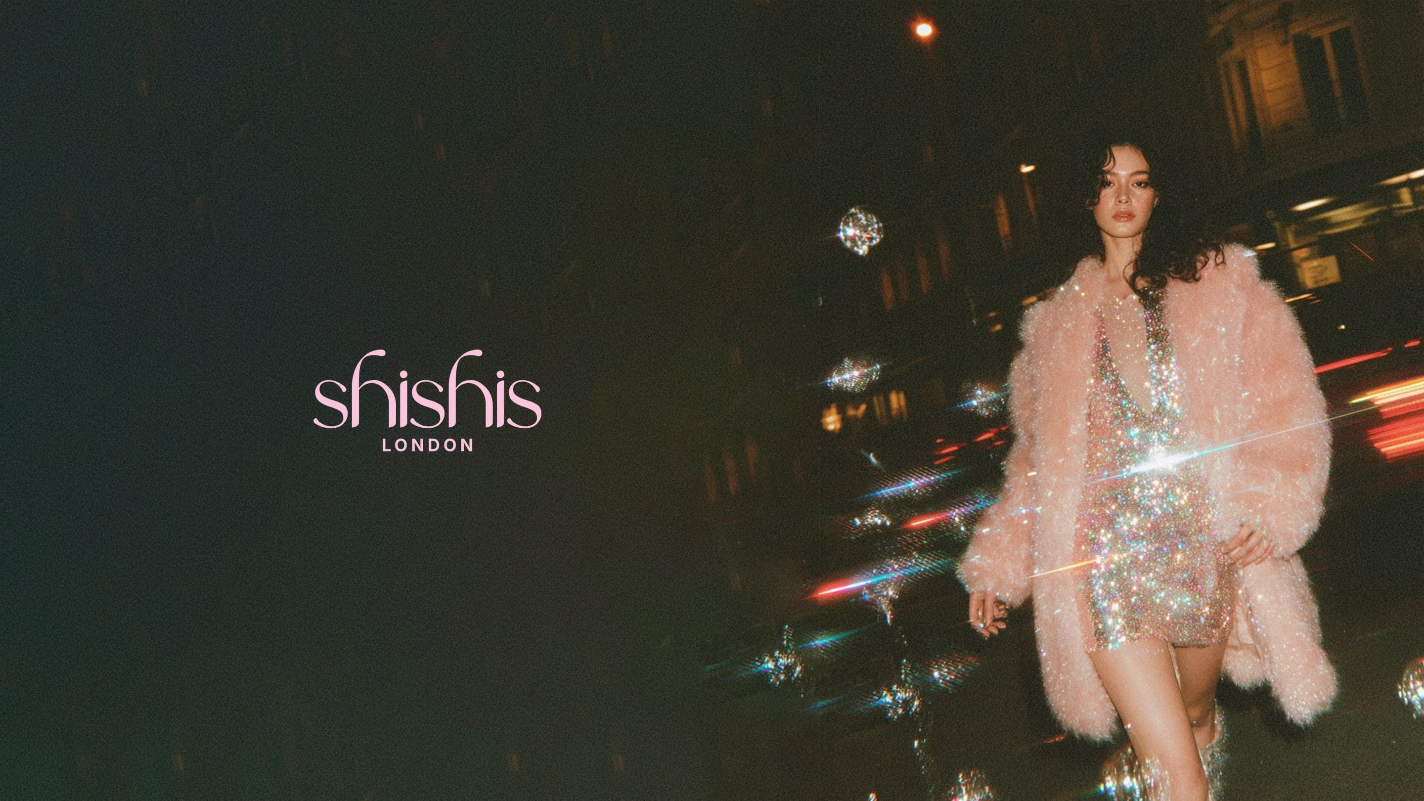 A woman in a pink fur coat and sequins on a street at night, the shishis London wordmark in the dark