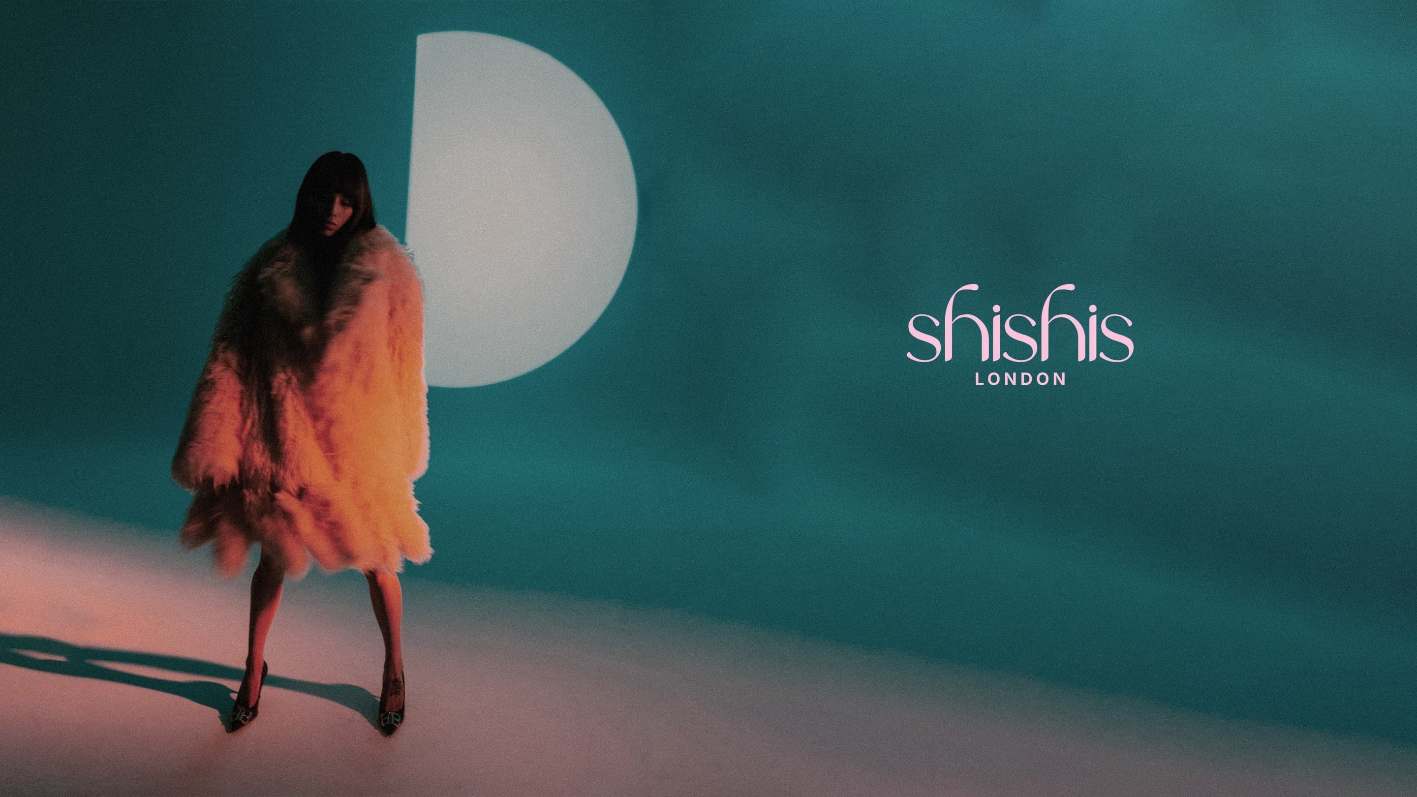 A woman in a fur coat lit orange beside a white moon on teal, the shishis London wordmark beside it