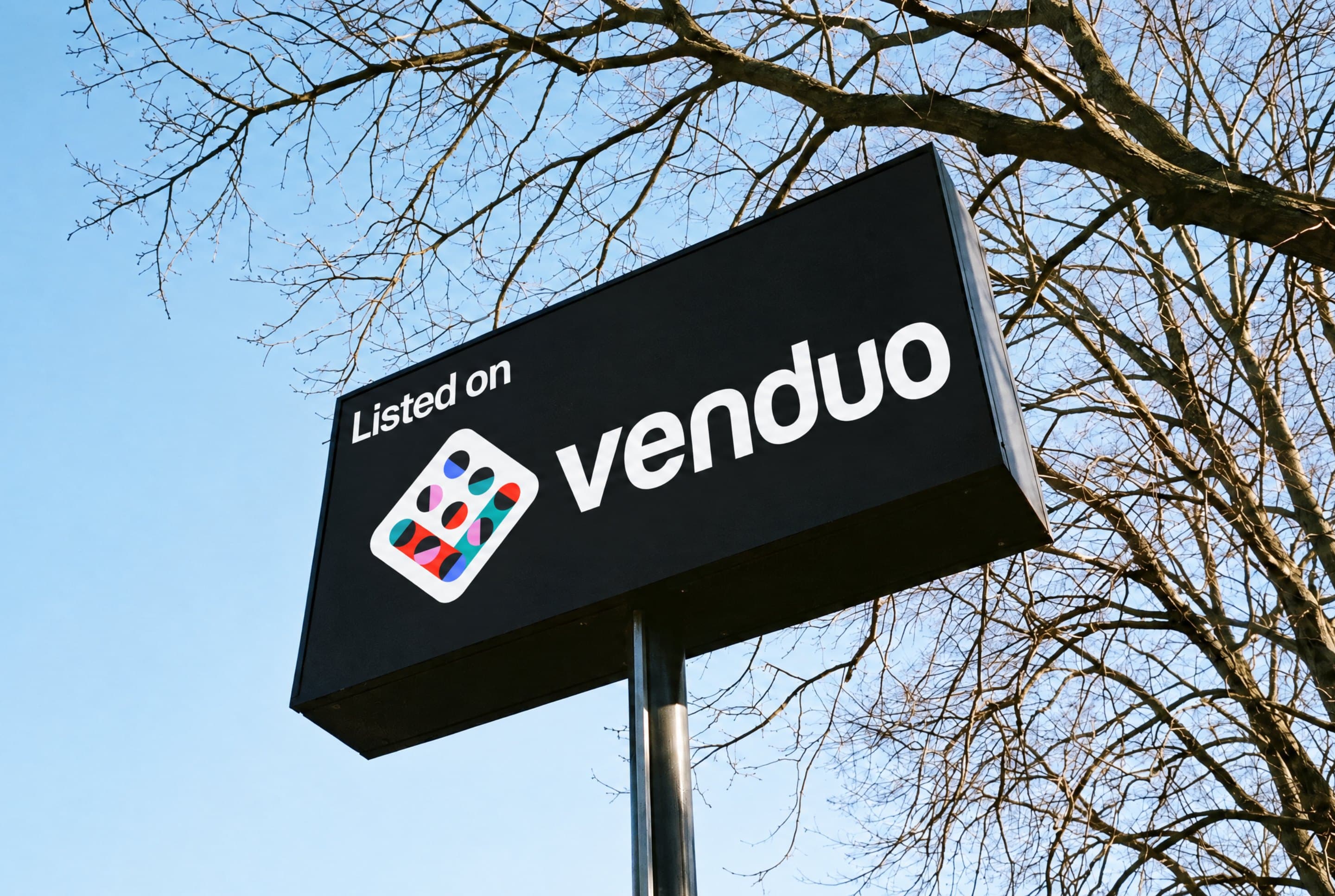 A Listed on venduo sign among bare branches against a blue sky